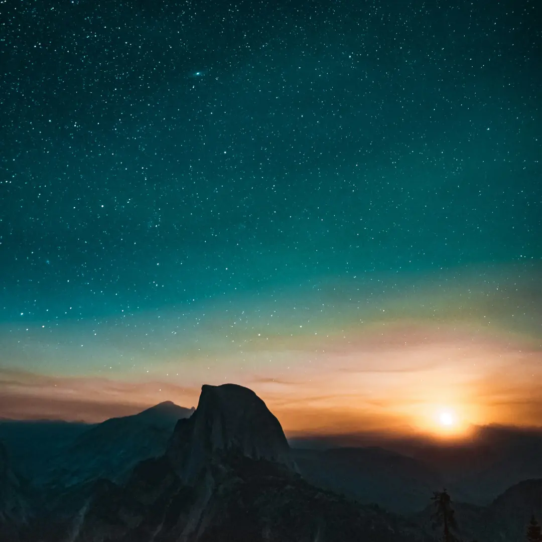 Majestic mountain peak in the foreground, bathed in the warm hues of a breathtaking sunset. The sky above reveals a celestial display of stars, creating a magical atmosphere under the evening glow.